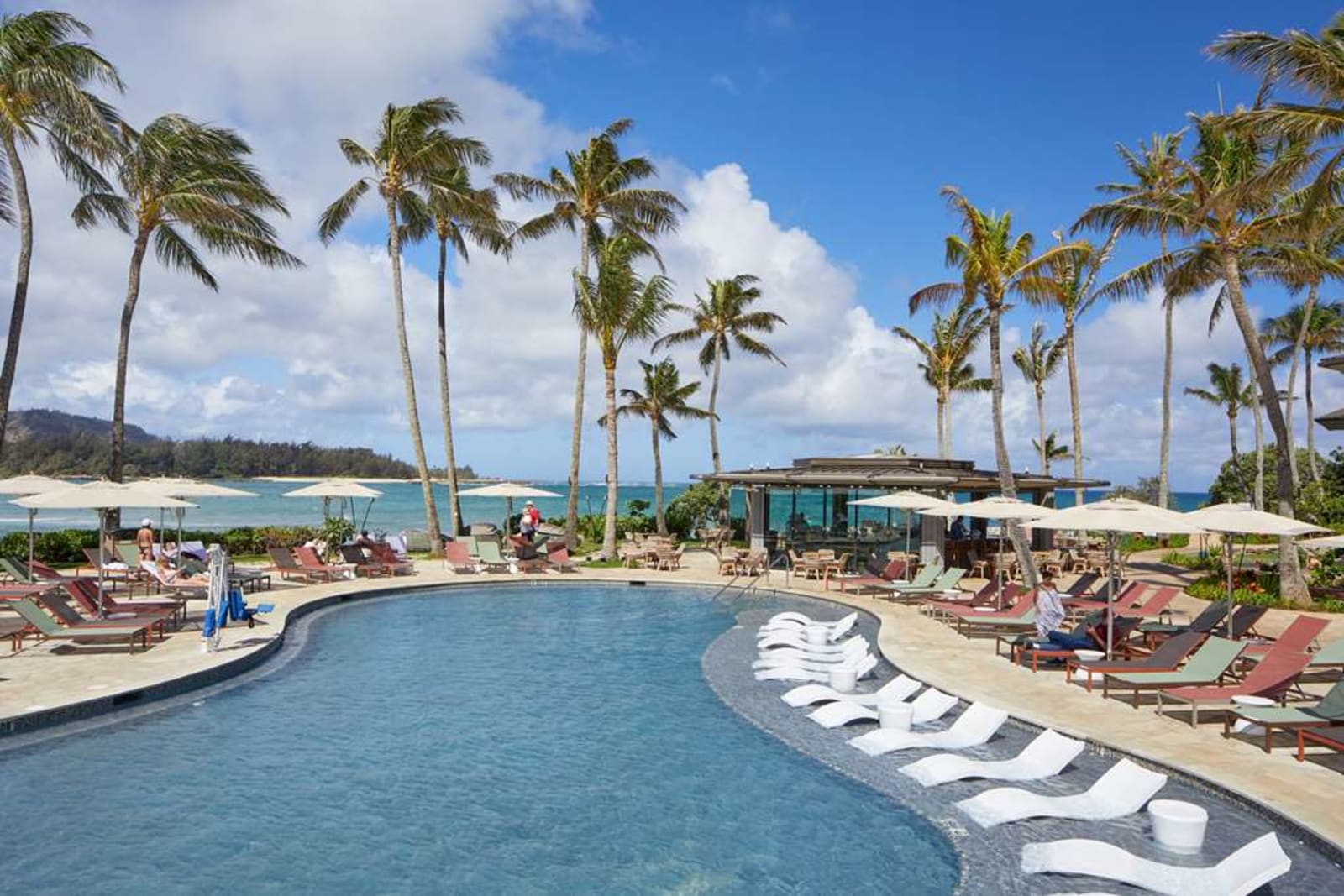 An aerial view of the main pool deck at The Ritz-Carlton O'ahu, Turtle Bay lined with palm trees and loungers