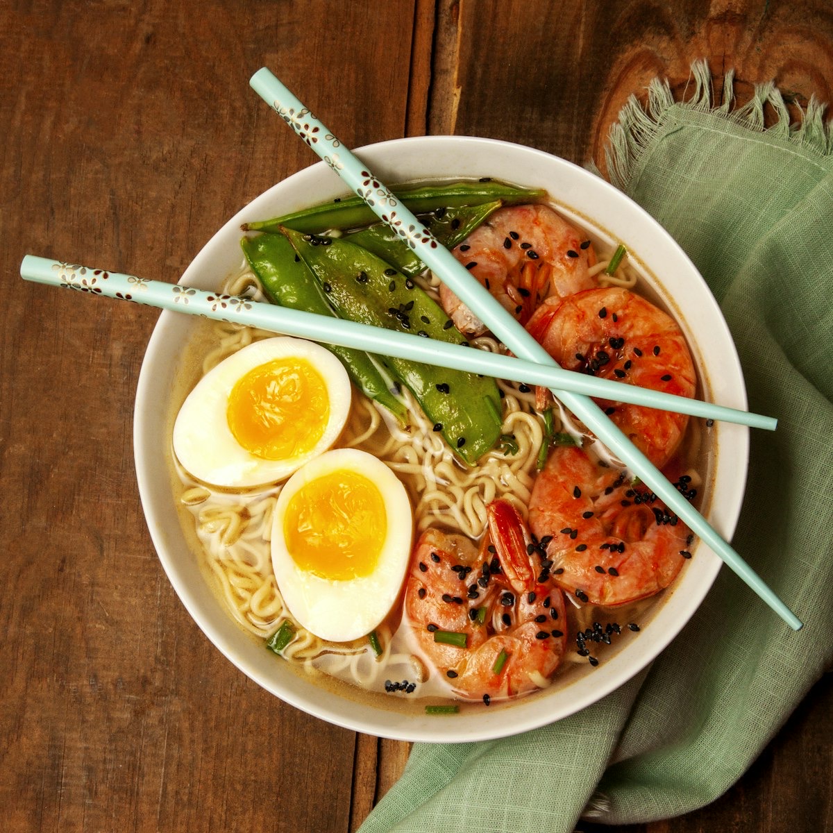 A warm bowl of Japanese ramen with a soft-boiled egg, shrimp, and snow peas